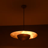 Nighttime image of brass disc pendant casting warm indirect light with an elegant layered dome silhouette