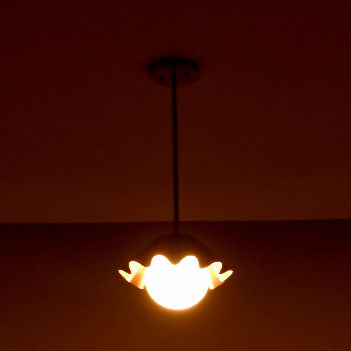 Single brass disc pendant light illuminating a dark room with warm indirect lighting.