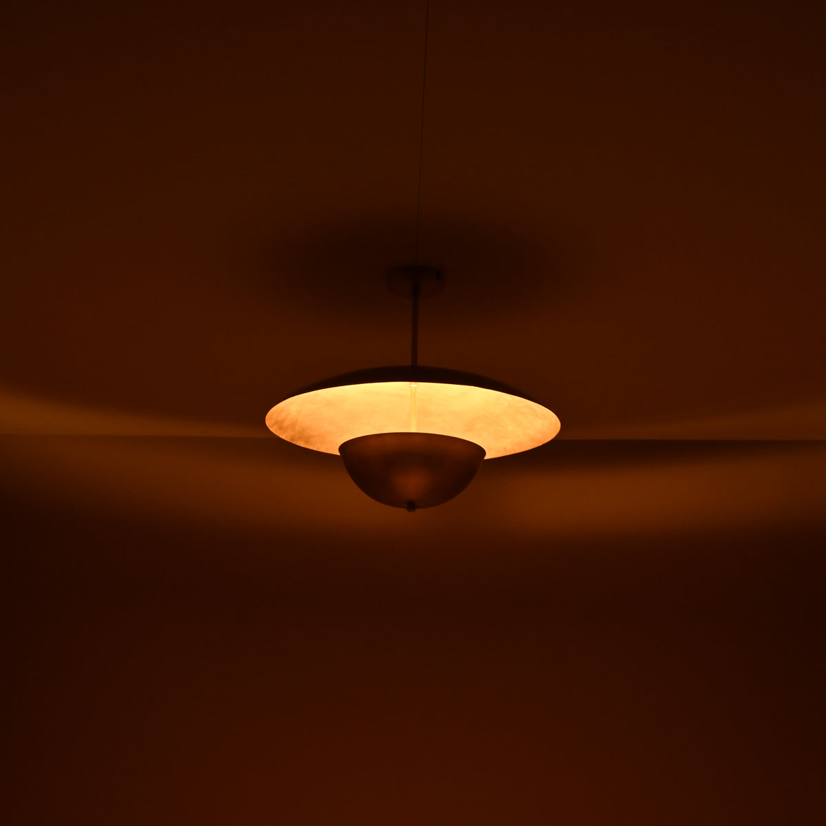 Warm ambient lighting from brass disc chandelier showing indirect uplight effect in a dim interior