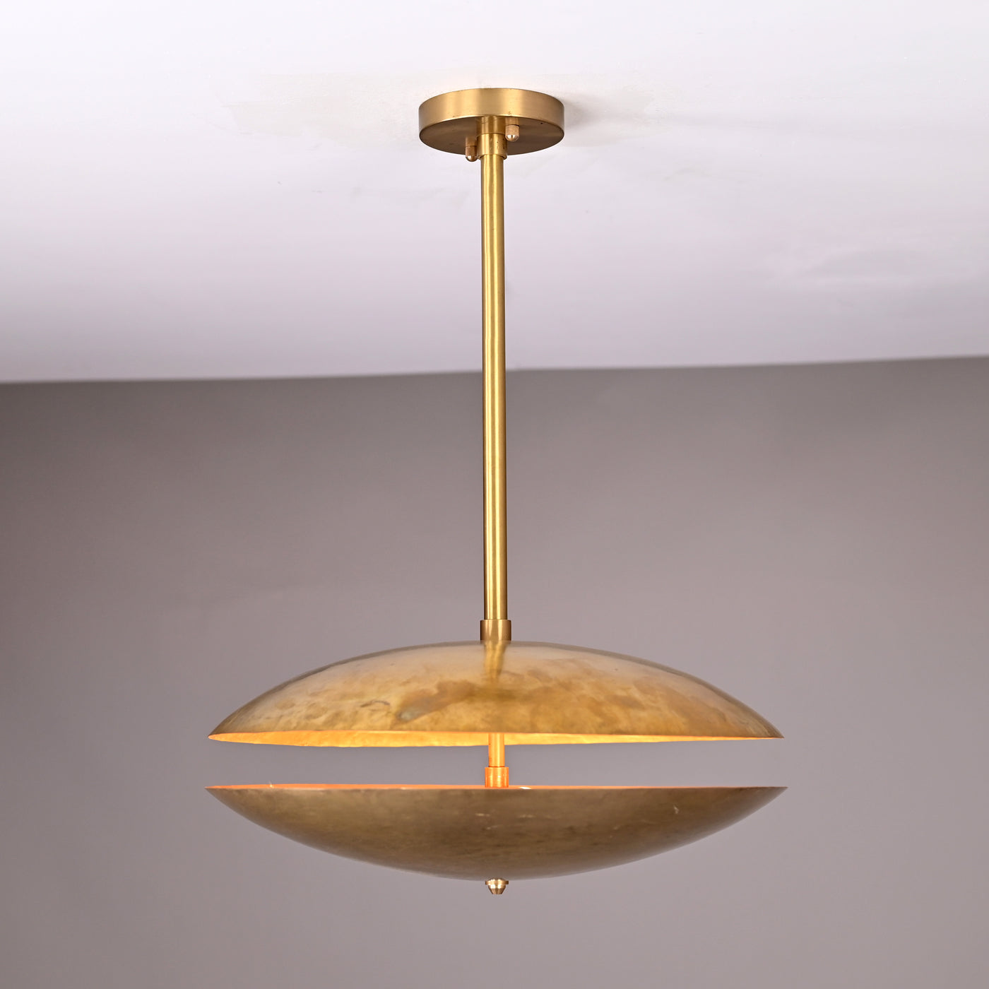 Handcrafted hammered brass disc pendant light with central rod suspension and warm indirect illumination, shown in a neutral interior setting.