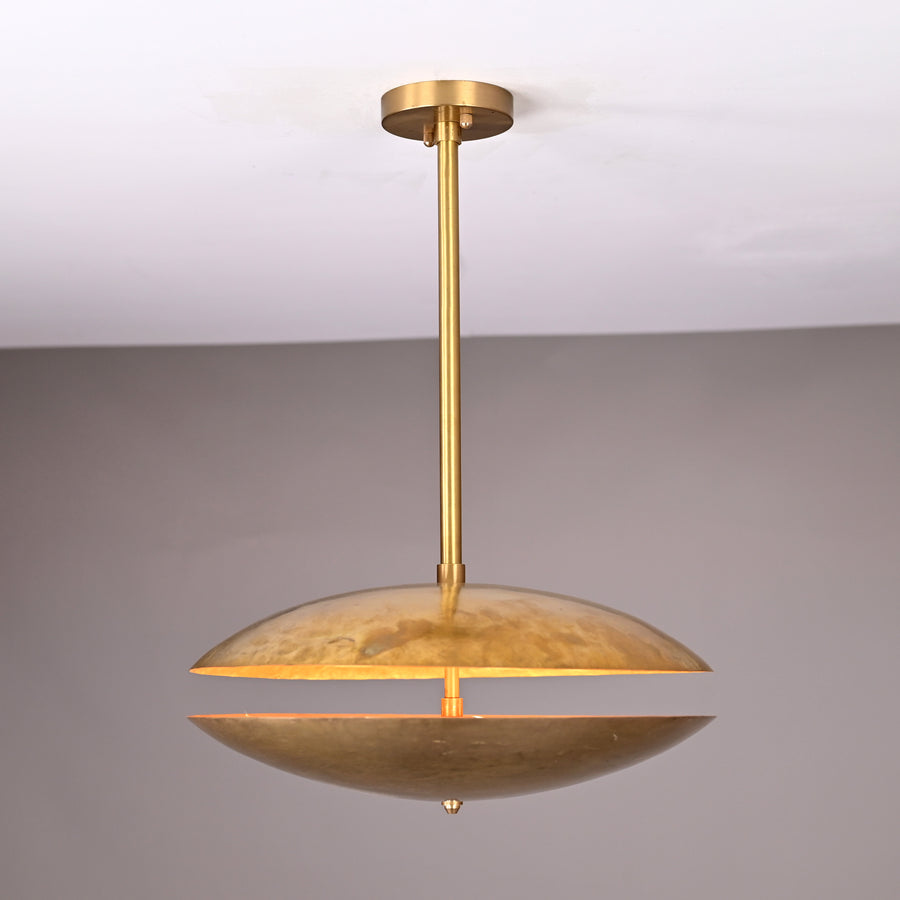 Handcrafted hammered brass disc pendant light with central rod suspension and warm indirect illumination, shown in a neutral interior setting.