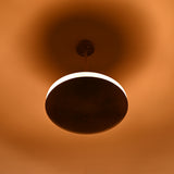 Brass disc pendant light photographed in low light, showing bright illuminated ring and soft ambient glow on ceiling and surroundings.