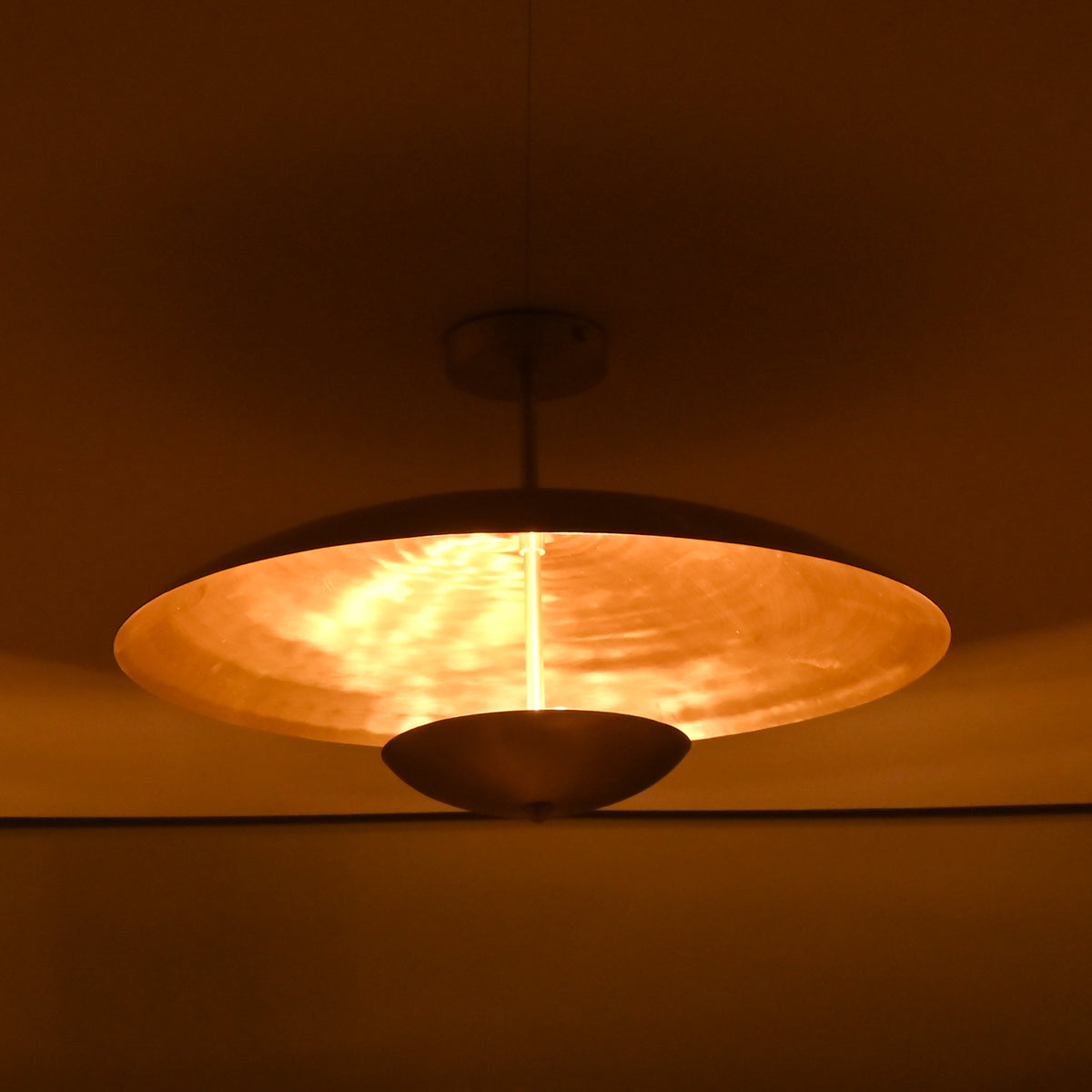 Side view of brass disc pendant light at night showing warm reflective glow and dual-disc structure
