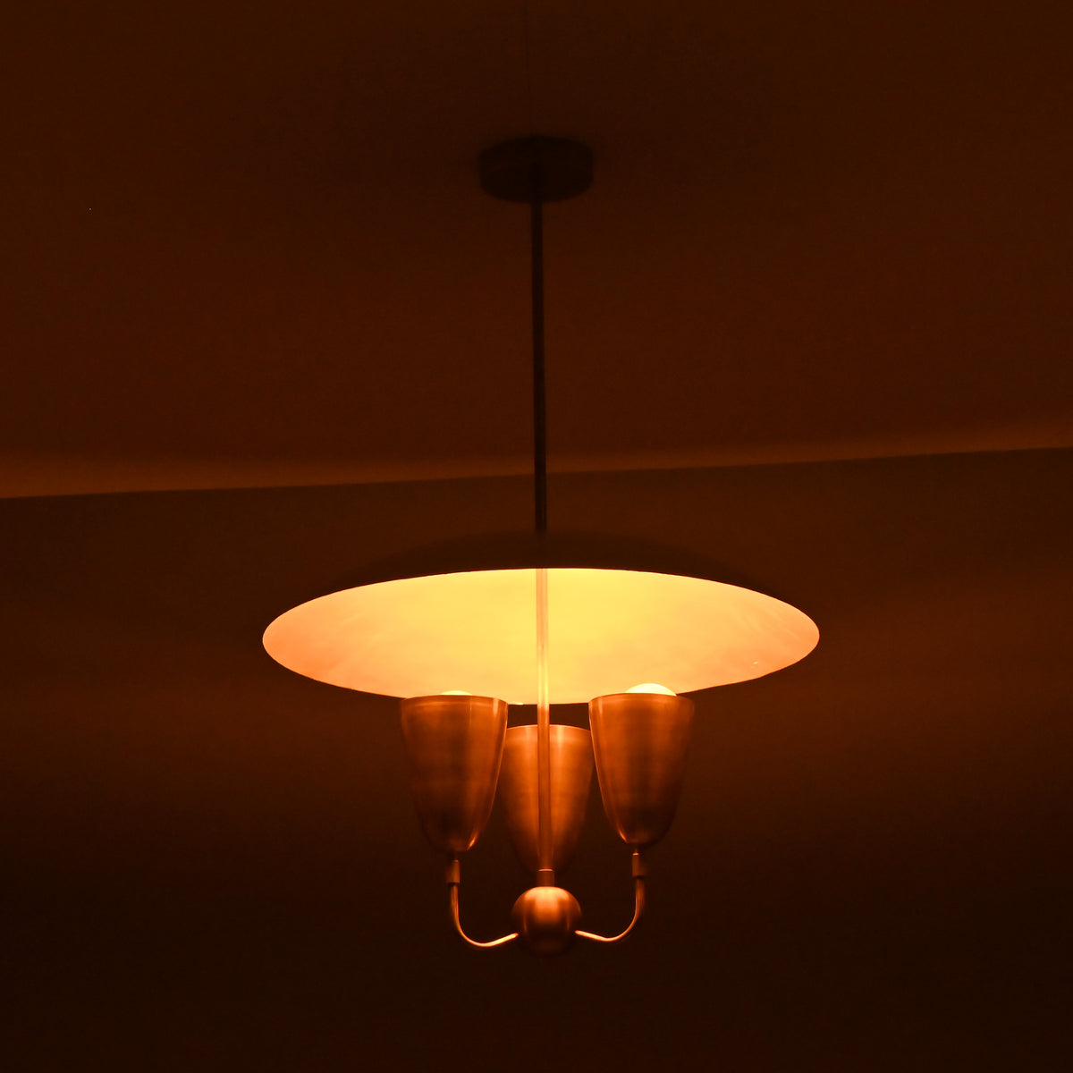 Evening view of brass dome pendant chandelier emitting warm indirect glow, mid-century brass ceiling fixture.