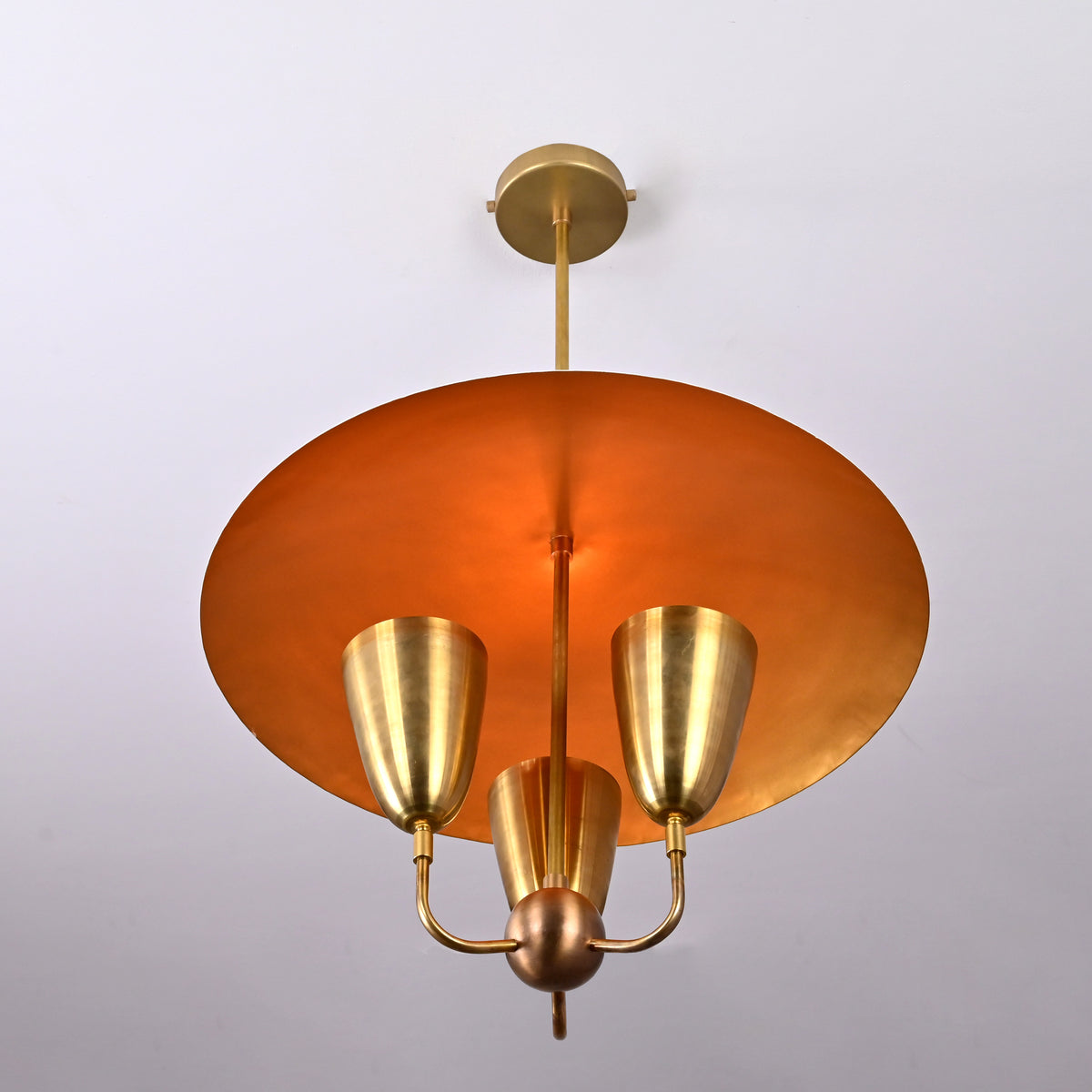 Warm-lit brass dome pendant chandelier glowing from below, revealing gold interior finish and three brass uplight cups.
