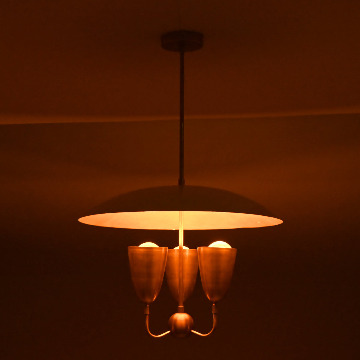 Warm ambient brass pendant chandelier with wide dome shade and three brass light cups creating soft atmospheric lighting.