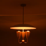 Warm ambient brass pendant chandelier with wide dome shade and three brass light cups creating soft atmospheric lighting.