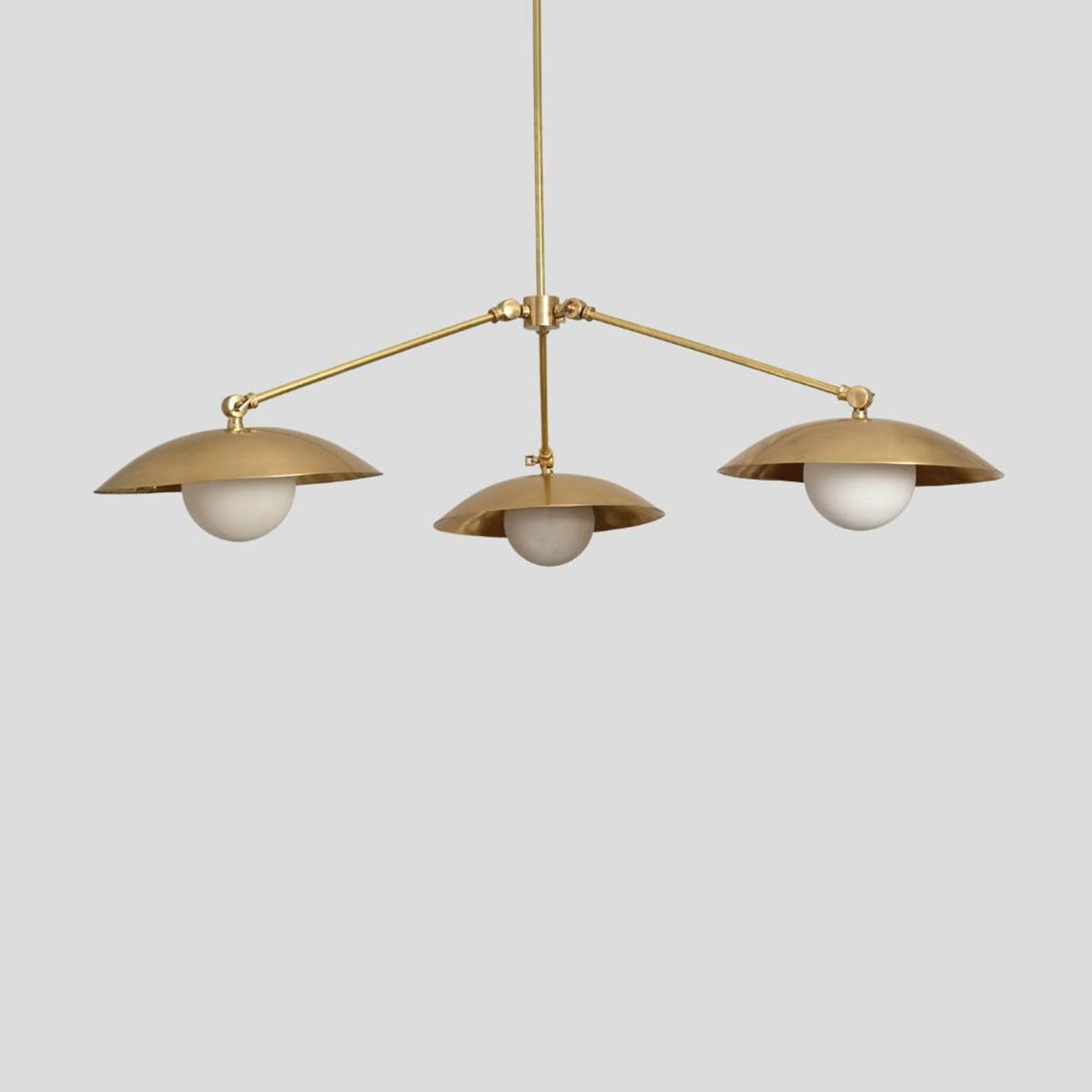 Elegant brass chandelier with three dome-shaped shades and globe bulbs, perfect for modern dining or living room lighting.