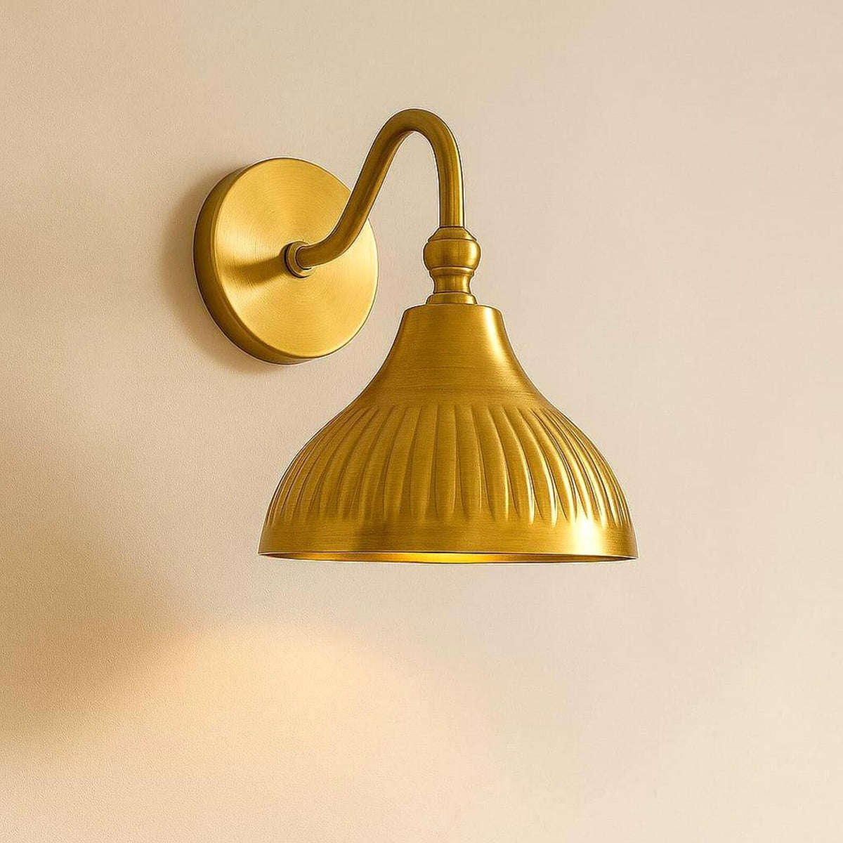 Solid brass dome wall light with fluted detailing emitting warm downward ambient glow on neutral wall.