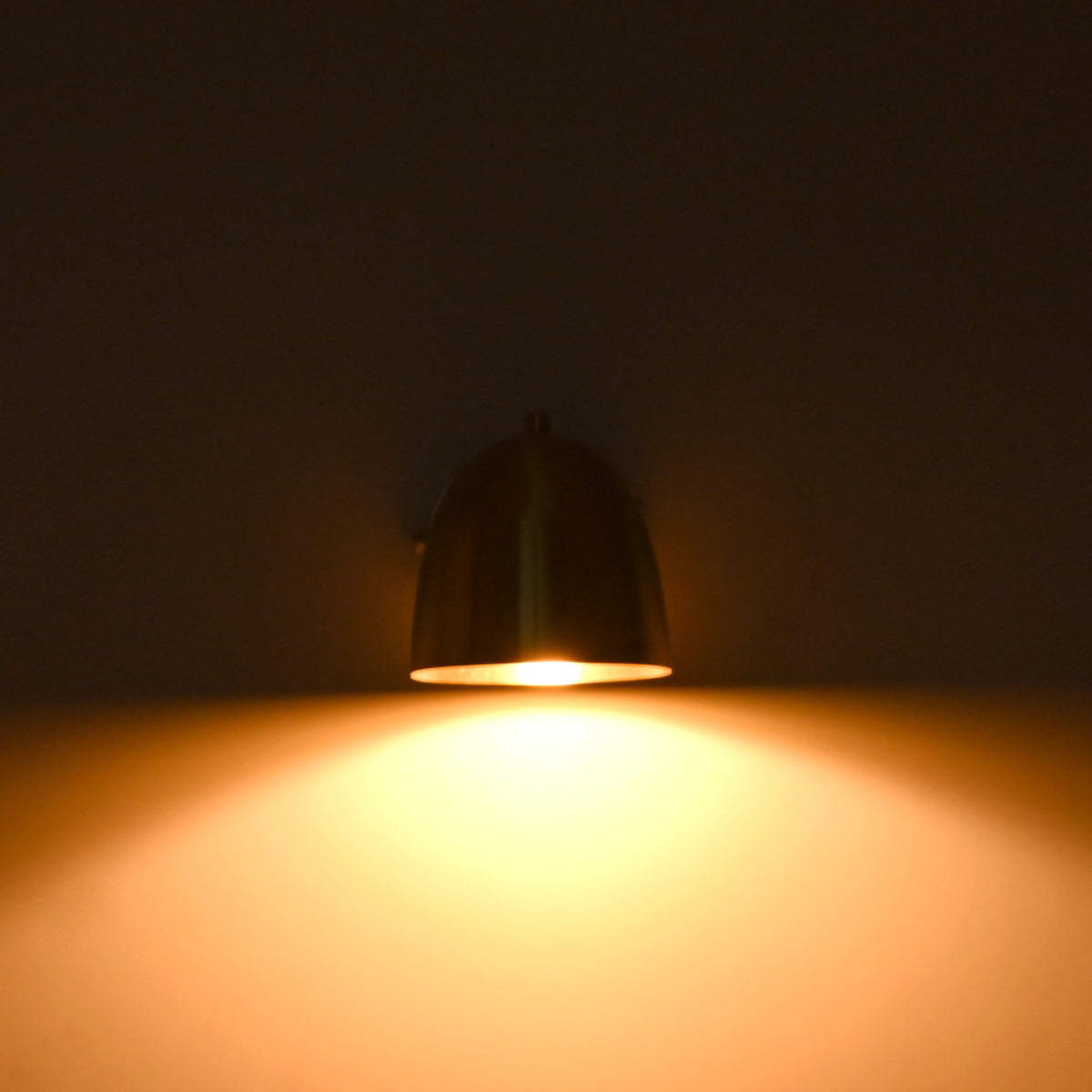 A dome-shaped wall sconce lamp with a dark metallic finish, glowing with a warm yellow light against a dark background.