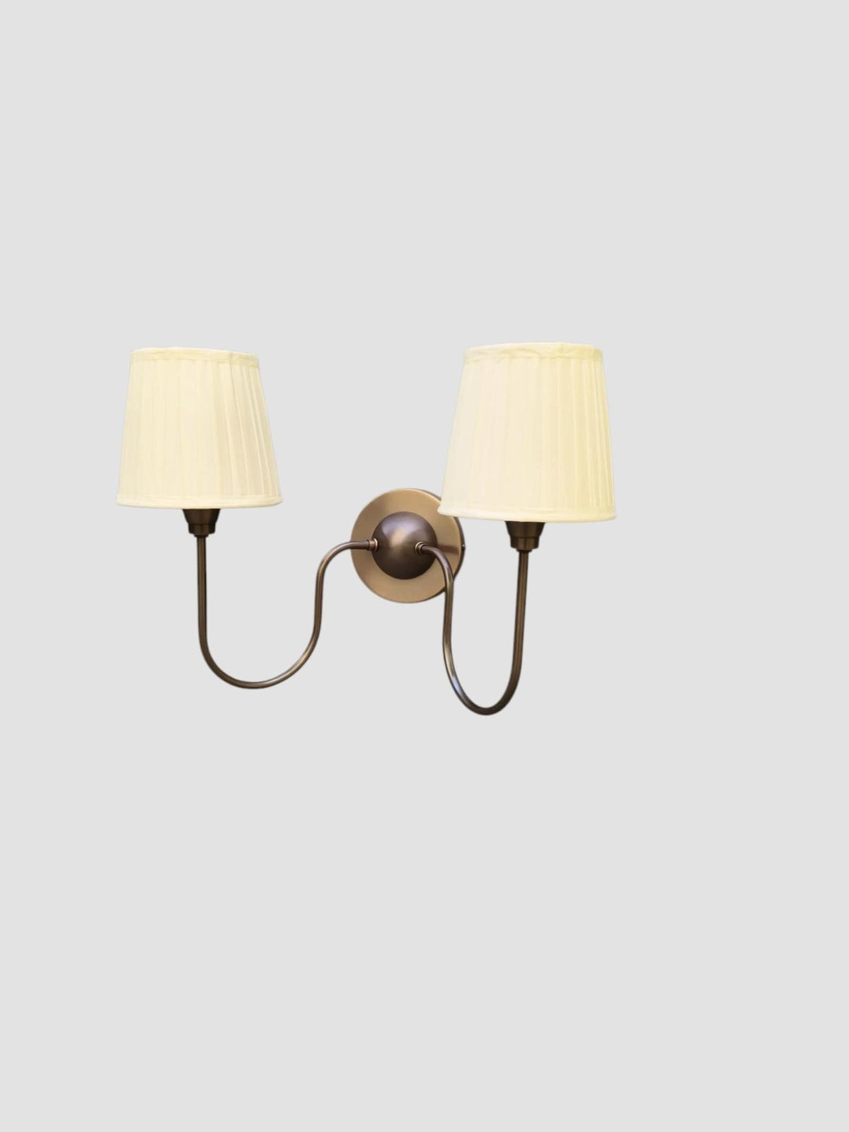 Angled side view of double arm wall sconce in blackened brass finish with pleated fabric shades