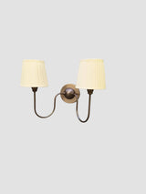 Angled side view of double arm wall sconce in blackened brass finish with pleated fabric shades