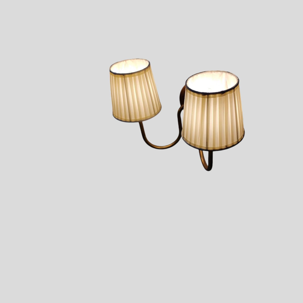 Angled perspective of brass wall sconce with pleated shades