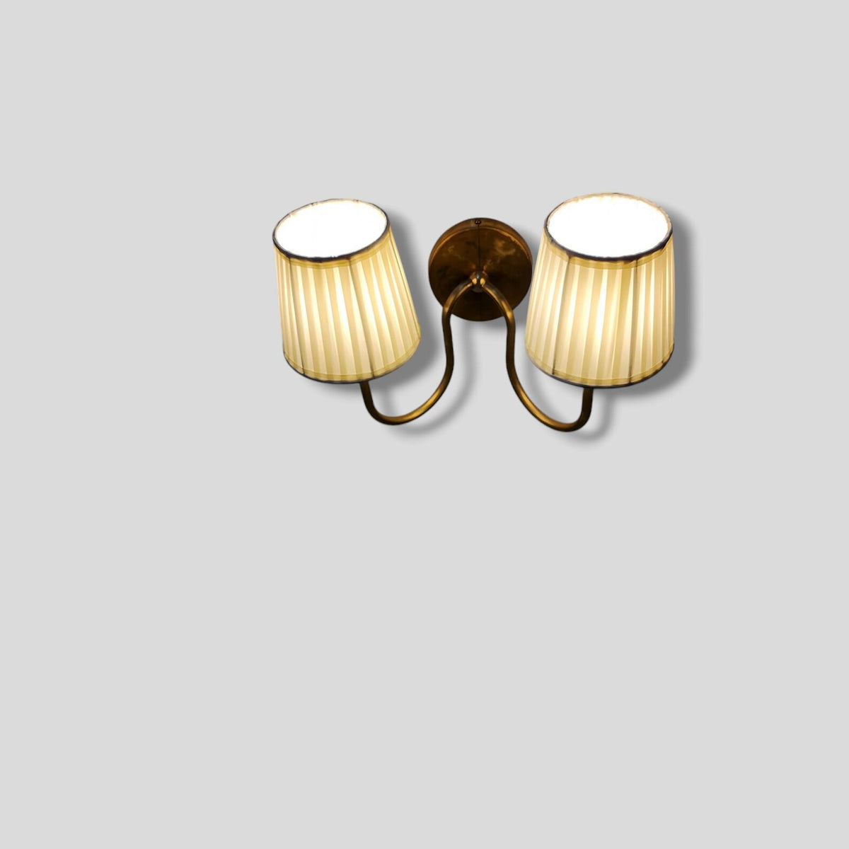 Top angled view of brass wall sconce with two pleated fabric shades
