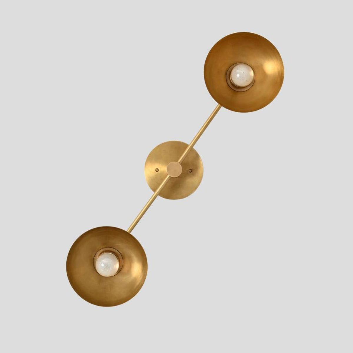 Diagonal view of handmade brass wall sconce with dual bowl-shaped shades, minimalist industrial design by Brass Leaf Studio.