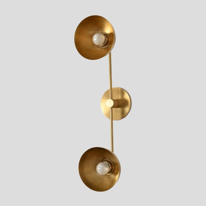 Vertical angle of handcrafted brass wall sconce featuring two bowl-shaped shades connected by a slim brass rod for minimalist lighting design.