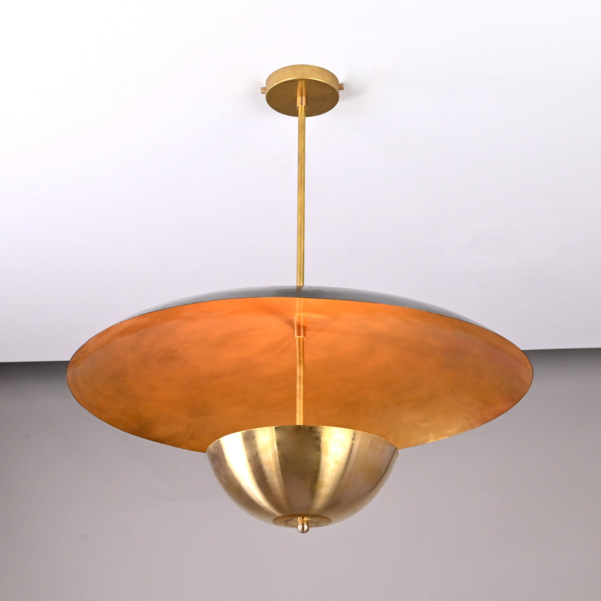 Underside view of brass dual-shade pendant showing warm reflective interior surface and sculptural bowl detail.