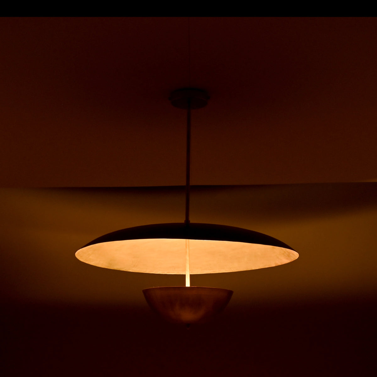 Warm-lit side view of dual-shade brass pendant casting soft ambient light through its sculptural dome and bowl.
