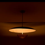 Warm-lit side view of dual-shade brass pendant casting soft ambient light through its sculptural dome and bowl.