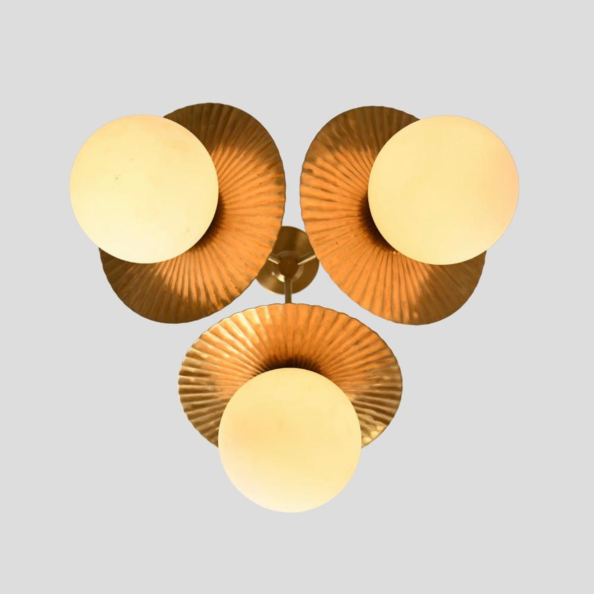 Top view of brass flushmount chandelier showing three frosted globes framed by sculpted fluted brass disc shades, modern handmade ceiling light.