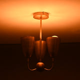 Brass flushmount chandelier with warm ambient lighting and sculpted triple cup design, mid-century modern fixture.