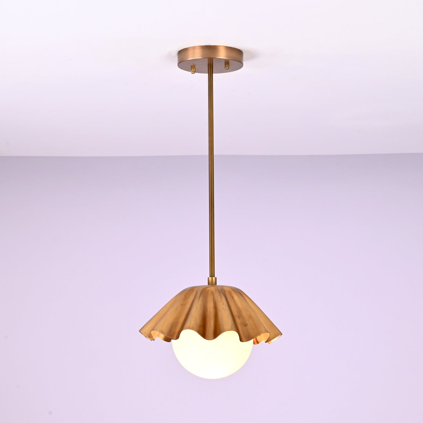 Minimalist brass fluted pendant light hanging straight with sculpted shade and glowing globe.