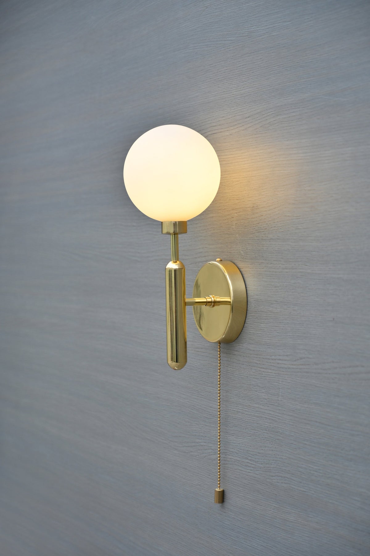 Close-up of polished brass globe wall light with white opal glass shade and sleek cylindrical arm