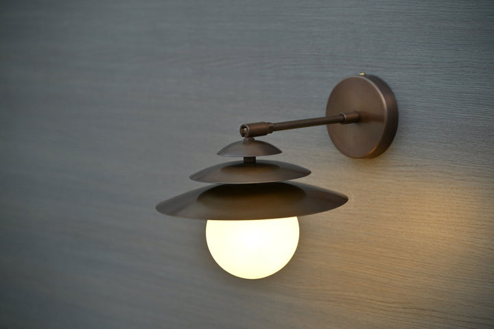 Angled perspective of handmade brass wall sconce with three layered shades and globe light diffuser