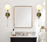 Pair of polished brass globe wall sconces installed beside bathroom mirror, creating soft ambient lighting