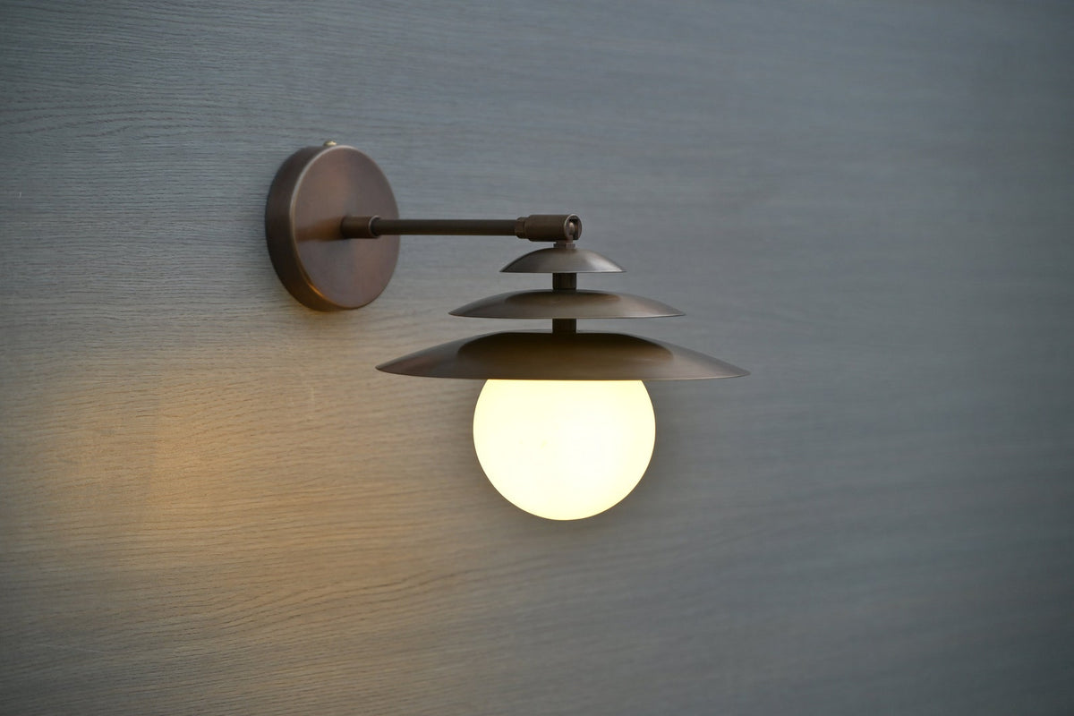 Side view of layered brass wall sconce with glowing globe diffuser, minimalist industrial wall light