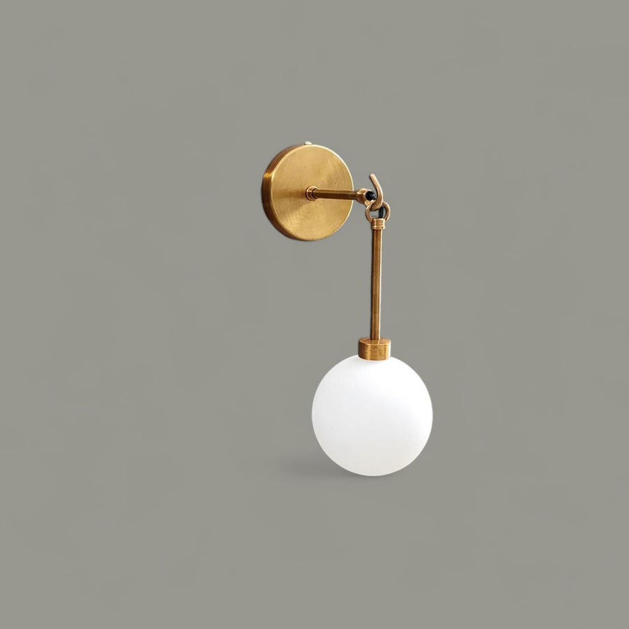 Modern brass wall sconce with frosted glass globe mounted on beige wall – handcrafted lighting by Brass Leaf Studio