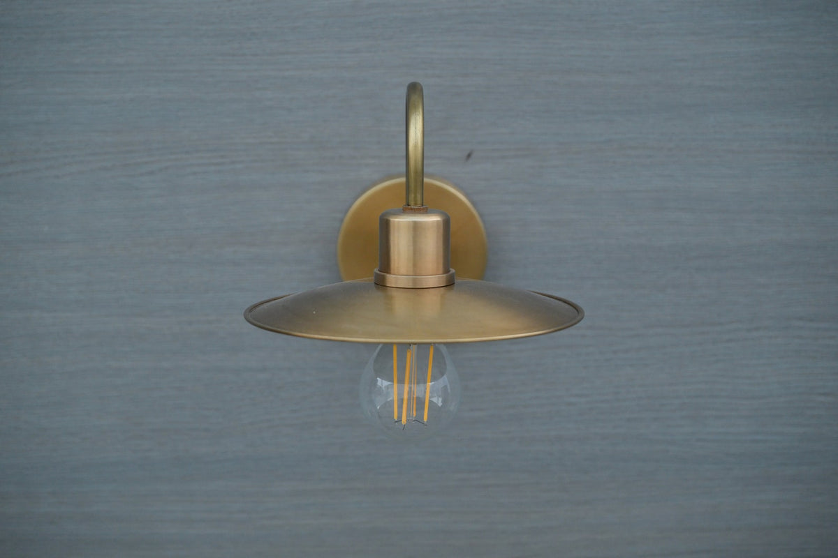 Front view of brass gooseneck wall light with wide brass shade and E26 bulb holder, perfect for industrial or modern interiors.