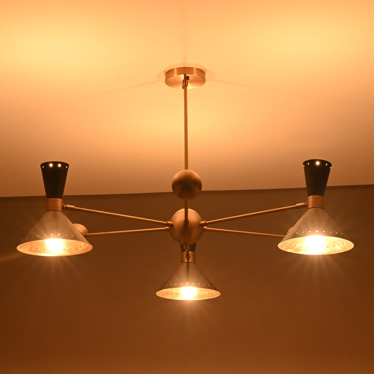 Warm-lit 3-light brass chandelier with cone shades, handcrafted in a mid-century modern industrial style.