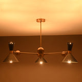 Warm glowing top-view image of a 3-light brass cone shade chandelier illuminating the ceiling with ambient light.