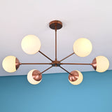 Six-light modern brass chandelier with spherical frosted glass globes and copper finish arms mounted on ceiling against blue wall.