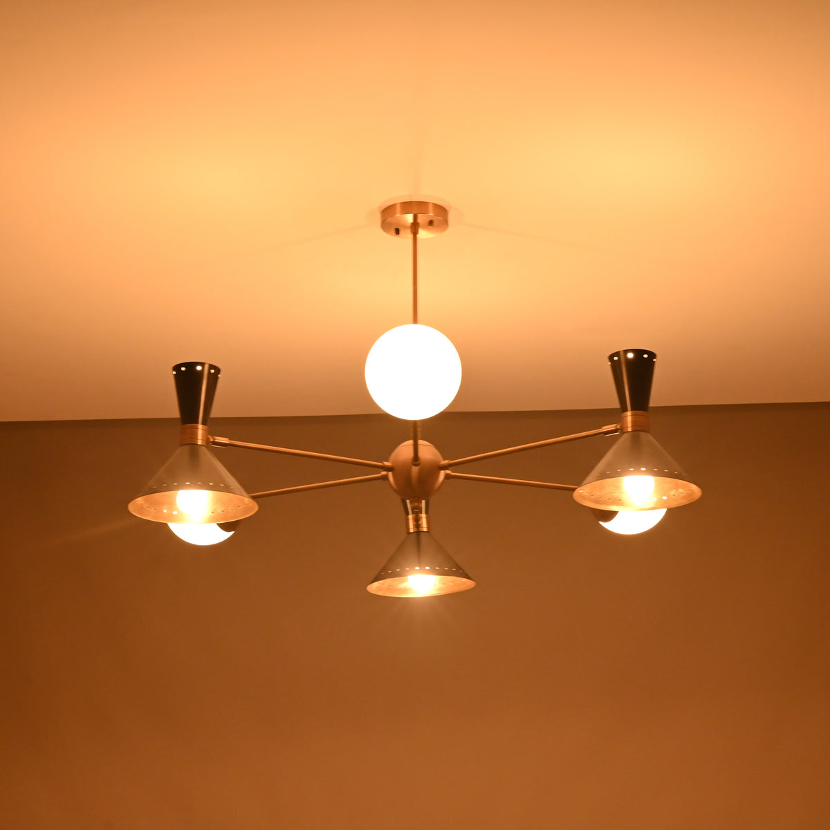 Warm glowing night view of a 9-light brass chandelier with cone shades and opal globes illuminating the ceiling.