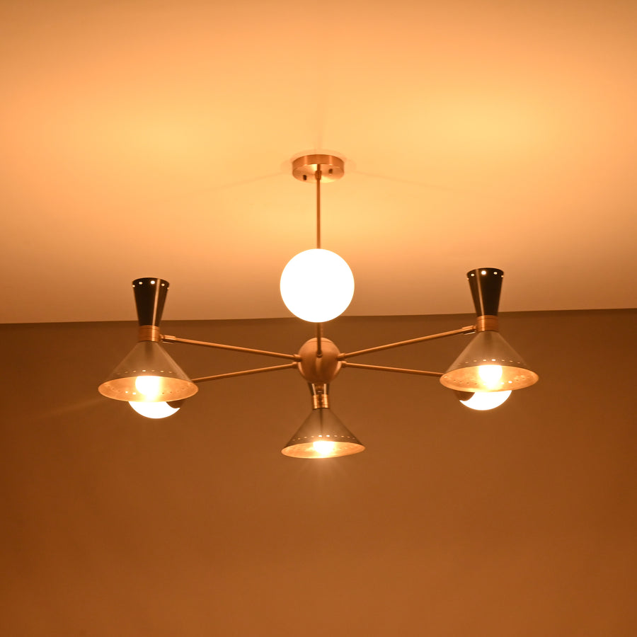 Front view of a 9-light brass chandelier featuring perforated cone shades and opal globes in a modern mid-century design.