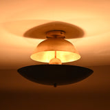Night view of a brass dome and matte black bowl flushmount light with glowing inner core and reflective brass sphere.