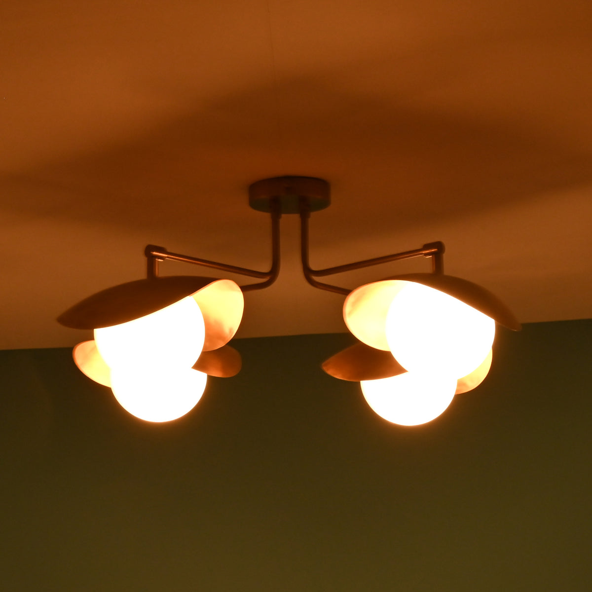 Side perspective of brass ceiling light at night highlighting curved bowl shades and warm illumination