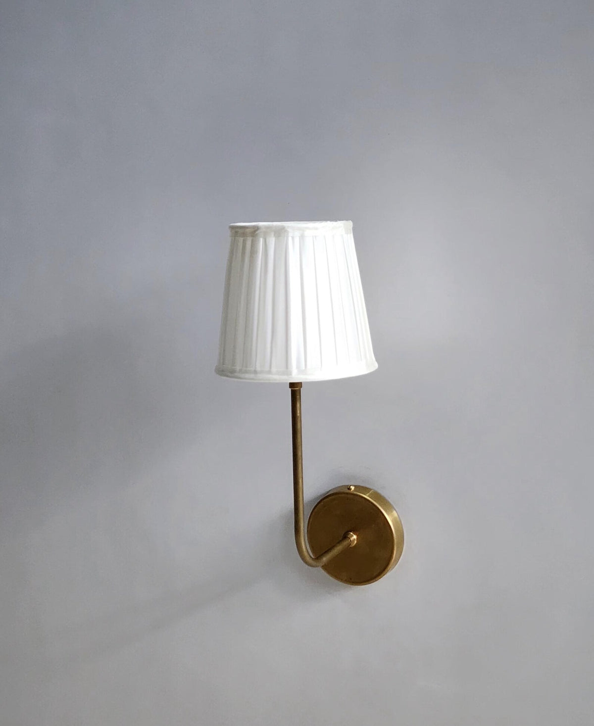 Elegant handcrafted brass wall lamp with white pleated shade, minimalist design by Brass Leaf Studio.