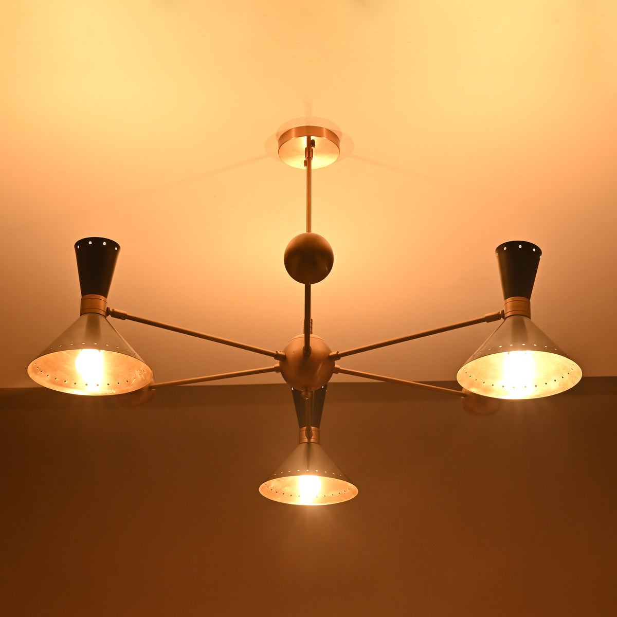 Illuminated industrial brass cone shade chandelier showing warm glowing perforated shades by Brass Leaf Studio.