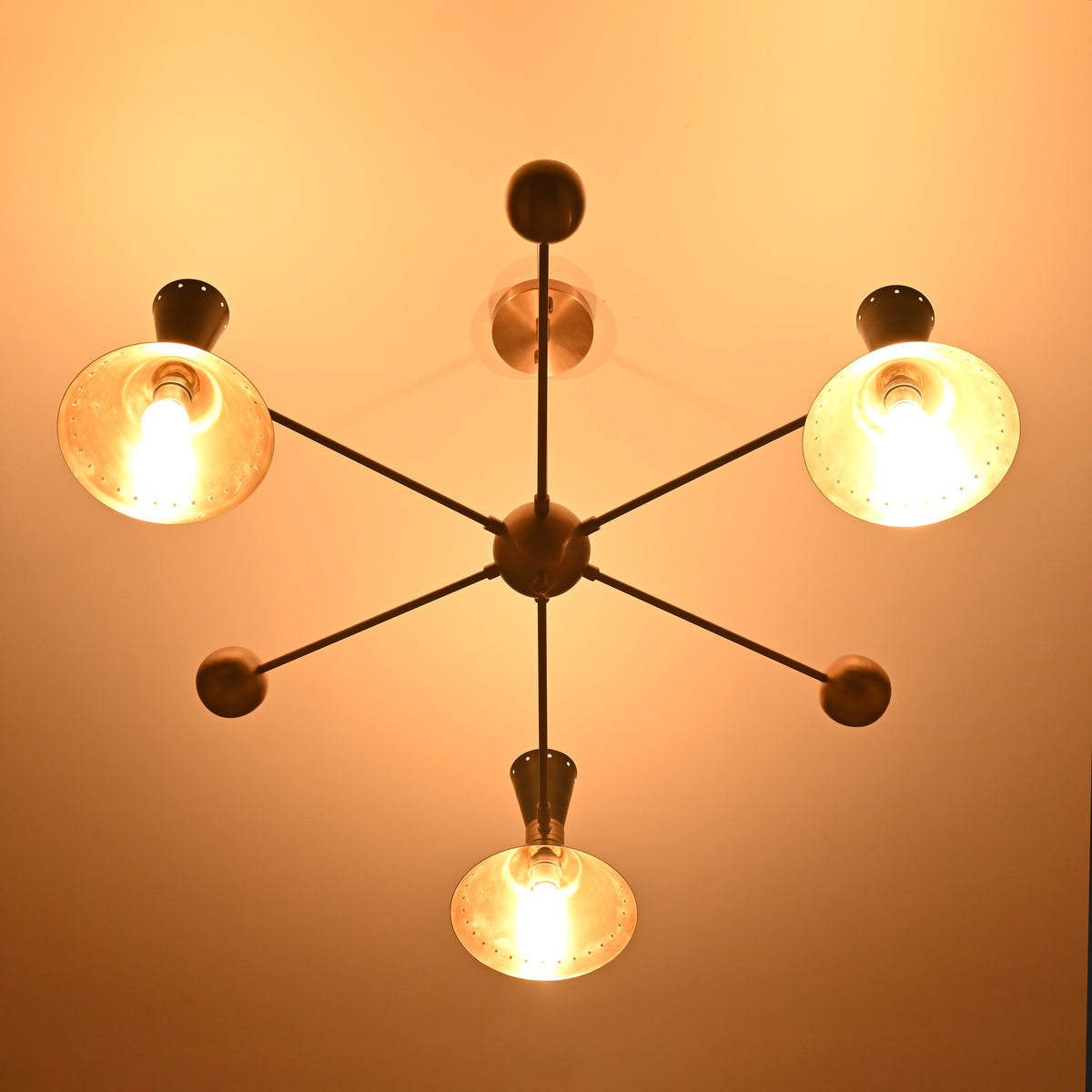 Night-view of a mid-century modern brass chandelier with cone shades emitting soft ambient lighting.