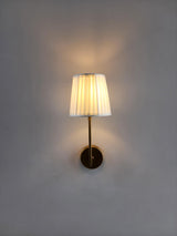 Minimalist brass wall sconce with glowing pleated shade creating soft ambient lighting.