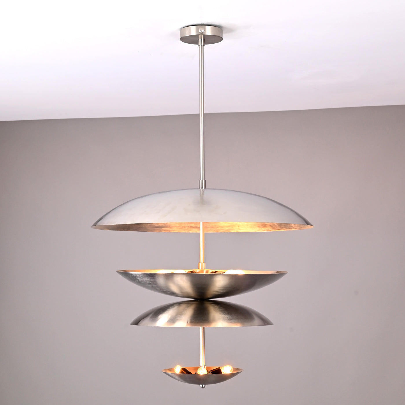Modern multi-tier brass disc chandelier with sculptural floating bowls and soft uplighting by Brass Leaf Studio.