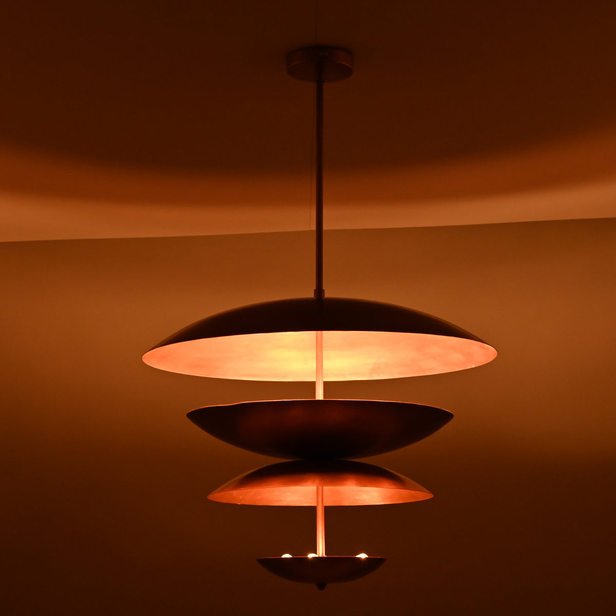 Modern tiered brass chandelier illuminated against a dark background, highlighting its floating bowl-shaped shades.