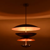 Modern tiered brass chandelier illuminated against a dark background, highlighting its floating bowl-shaped shades.