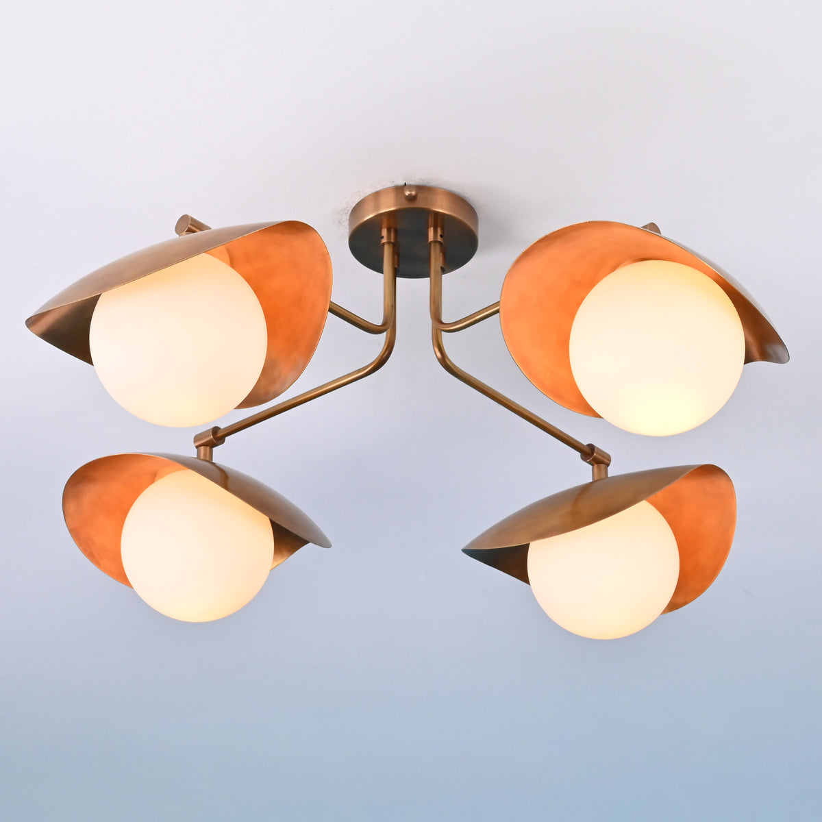 Symmetrical view of solid brass ceiling light featuring four opal globes and curved brass shades
