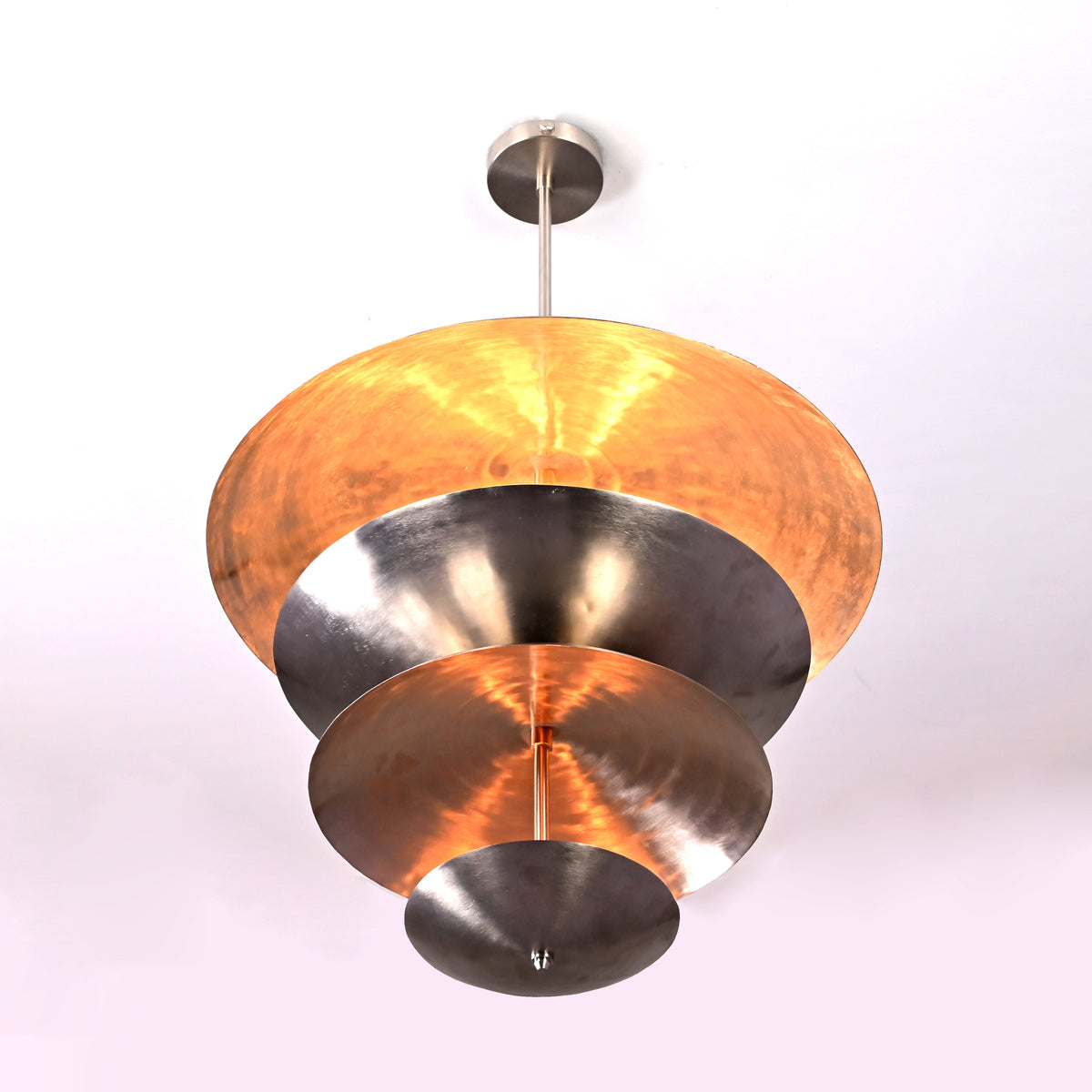 Bottom view of a sculptural tiered disc chandelier, showcasing concentric reflective brass discs illuminated from within.