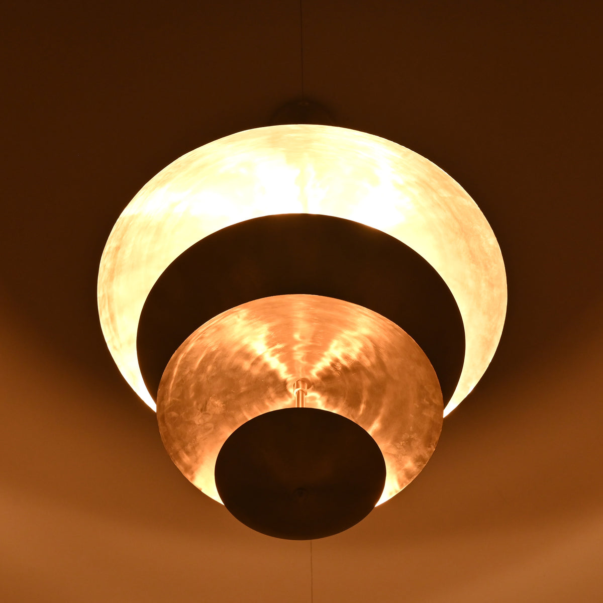 Warm ambient view of a tiered bowl-disc chandelier featuring layered sculptural metal shades by Brass Leaf Studio.