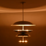 Warm glowing view of a tiered disc brass pendant light with layered metallic shades handcrafted by Brass Leaf Studio.
